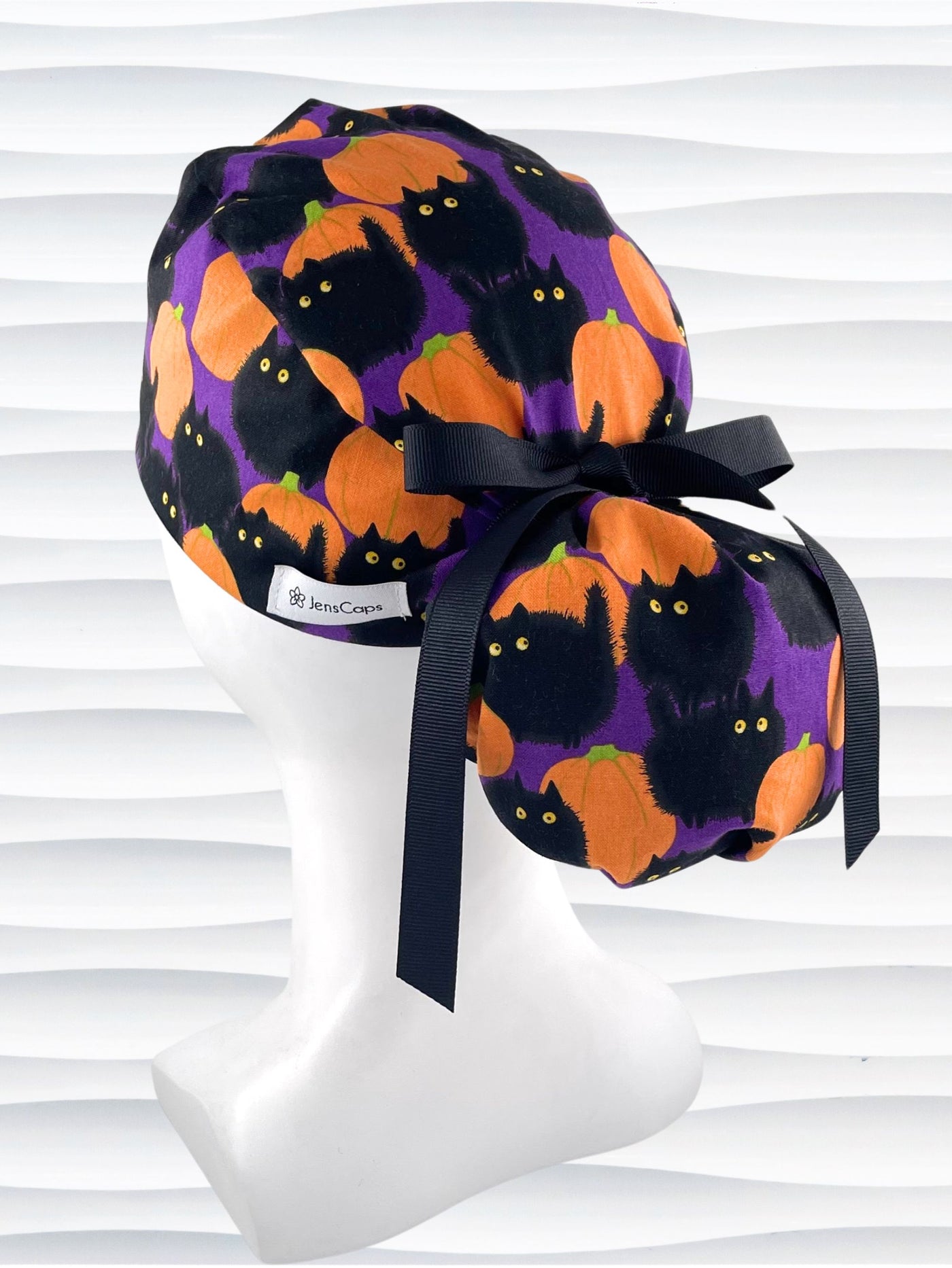 Ponytail style surgical scrub cap hat with puffy black cats and orange pumpkins all over this purple background cotton fabric.