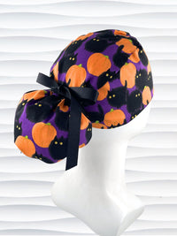 Ponytail style surgical scrub cap hat with puffy black cats and orange pumpkins all over this purple background cotton fabric.