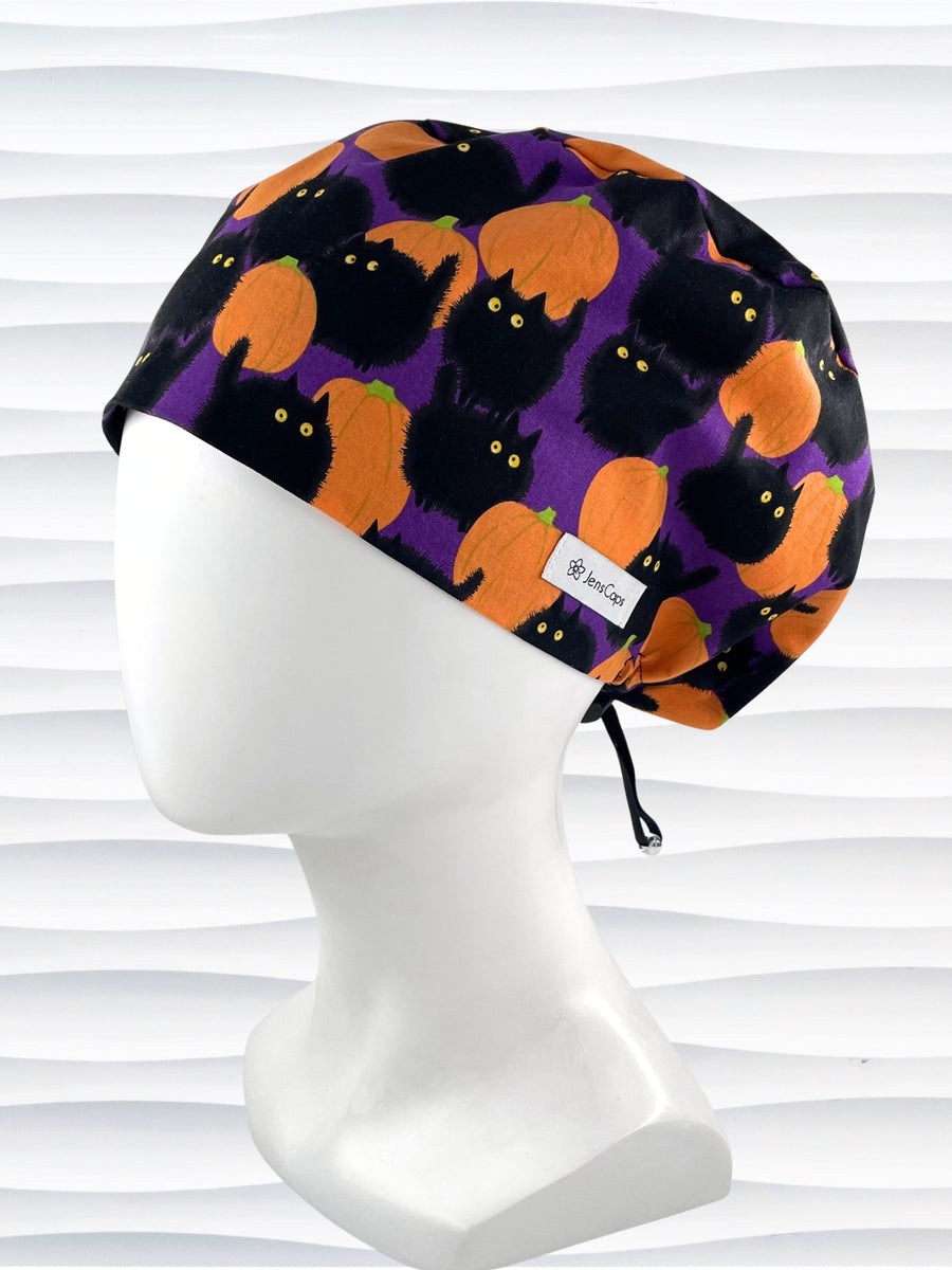 Euro Pixie style surgical scrub cap by JensCaps with black cats and orange pumpkins all over a purple background and displayed on a mannequin head