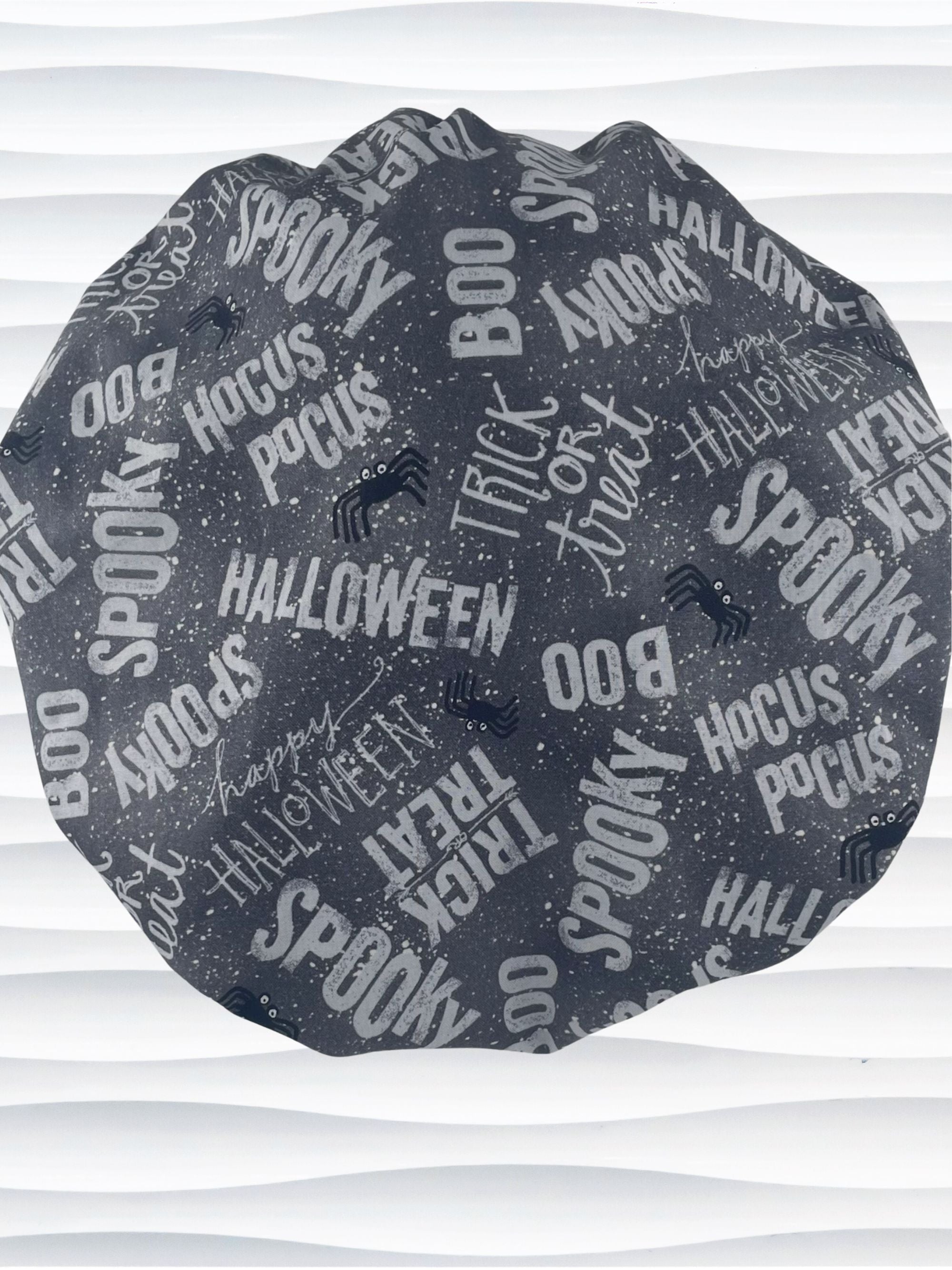 Bouffant style surgical scrub cap by JensCaps with halloween words in white and light gray and black spiders all over gray cotton fabric and displayed on a mannequin head.