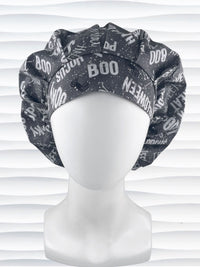 Bouffant style surgical scrub cap by JensCaps with halloween words in white and light gray and black spiders all over gray cotton fabric and displayed on a mannequin head.