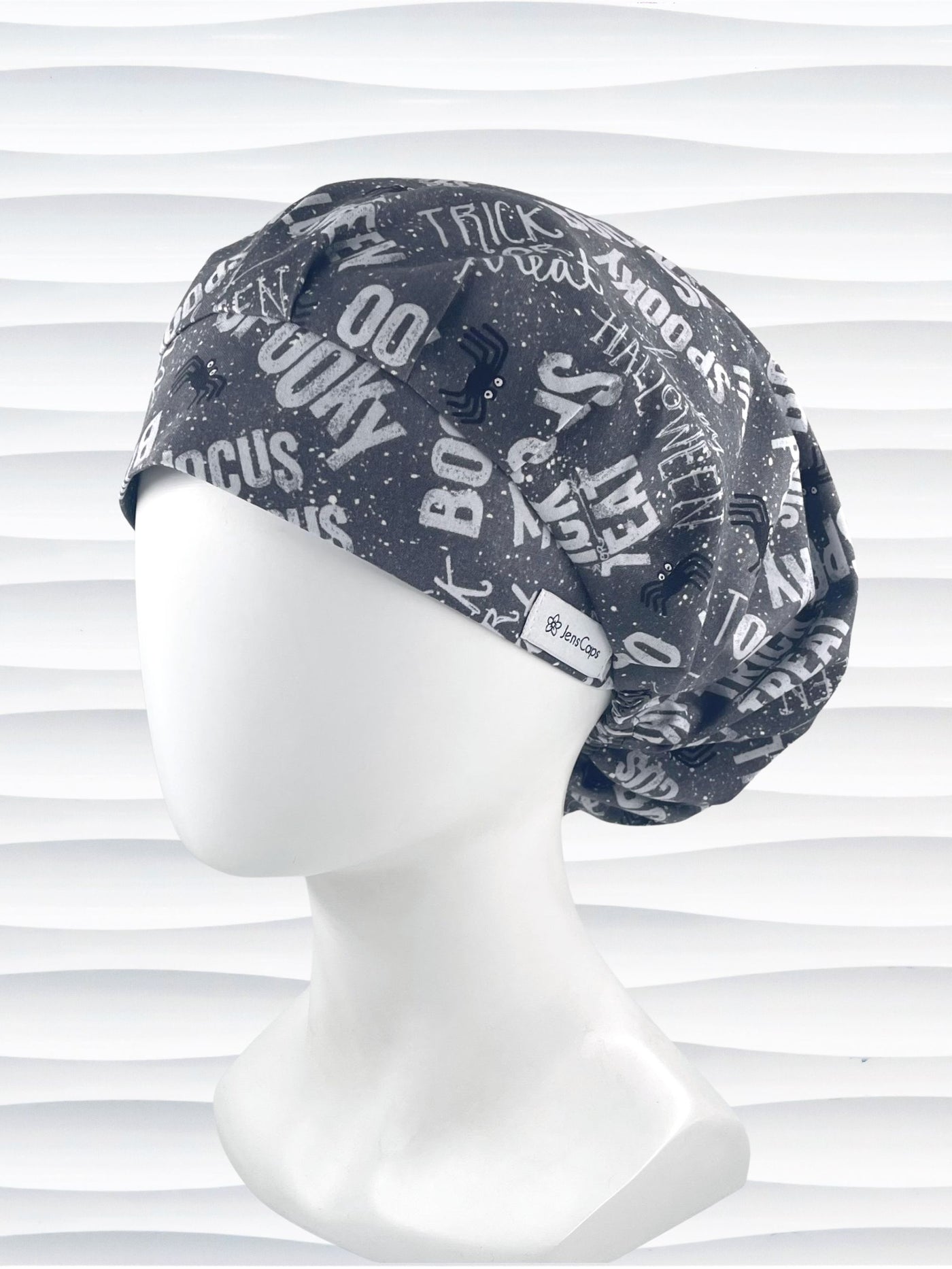 Bouffant style surgical scrub cap by JensCaps with halloween words in white and light gray and black spiders all over gray cotton fabric and displayed on a mannequin head.