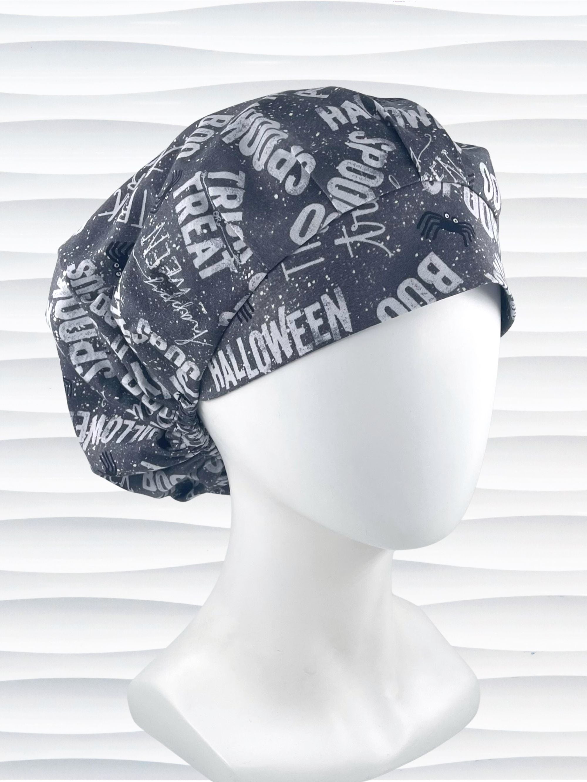 Bouffant style surgical scrub cap by JensCaps with halloween words in white and light gray and black spiders all over gray cotton fabric and displayed on a mannequin head.