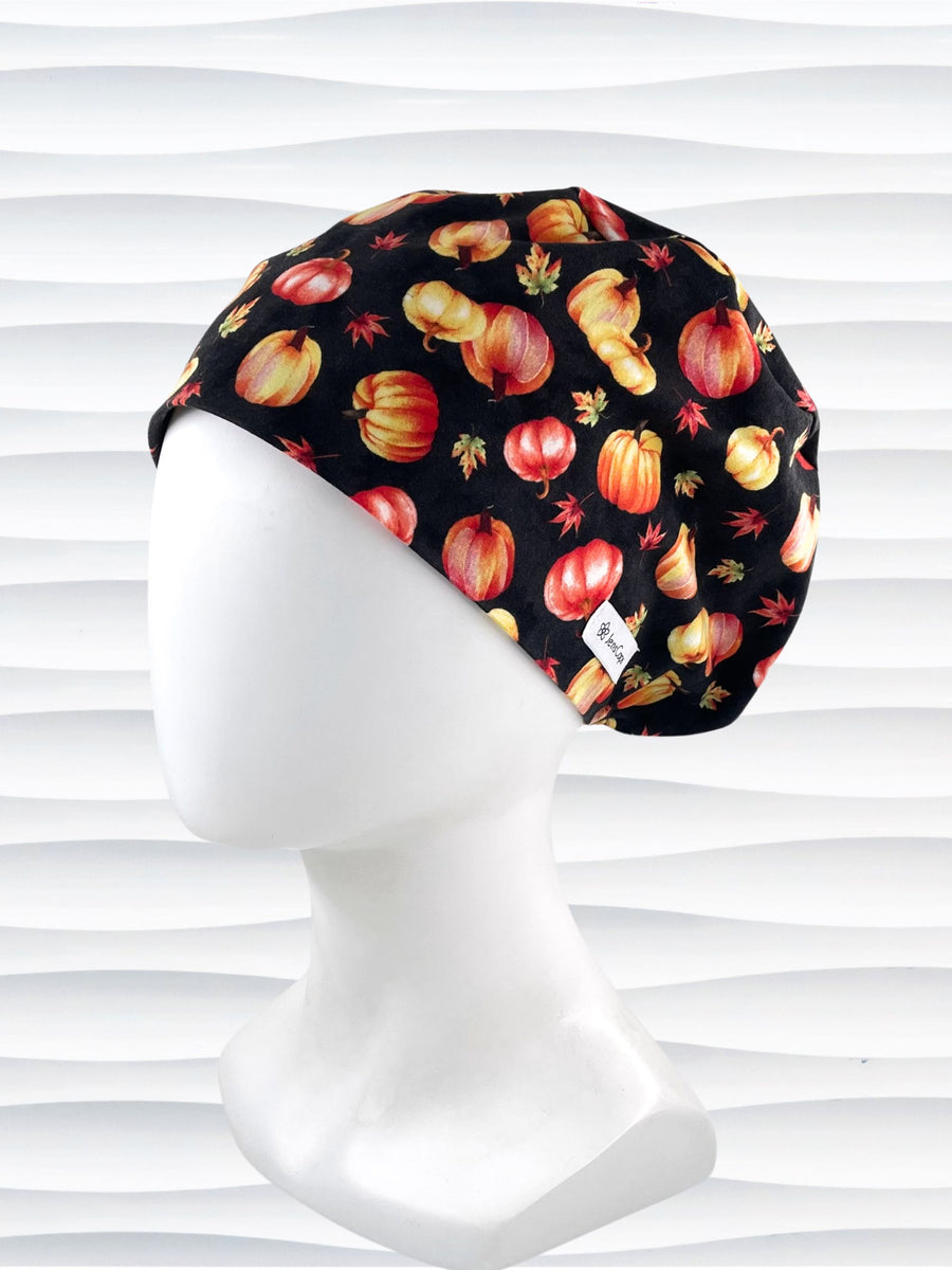 Pixie Euro style surgical scrub cap hat with orange and yellow pumpkins and leaves tossed on black premium fabric.