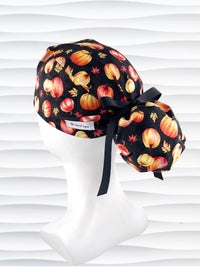 Ponytail style surgical scrub cap hat with orange and yellow pumpkins and leaves tossed on black premium fabric.