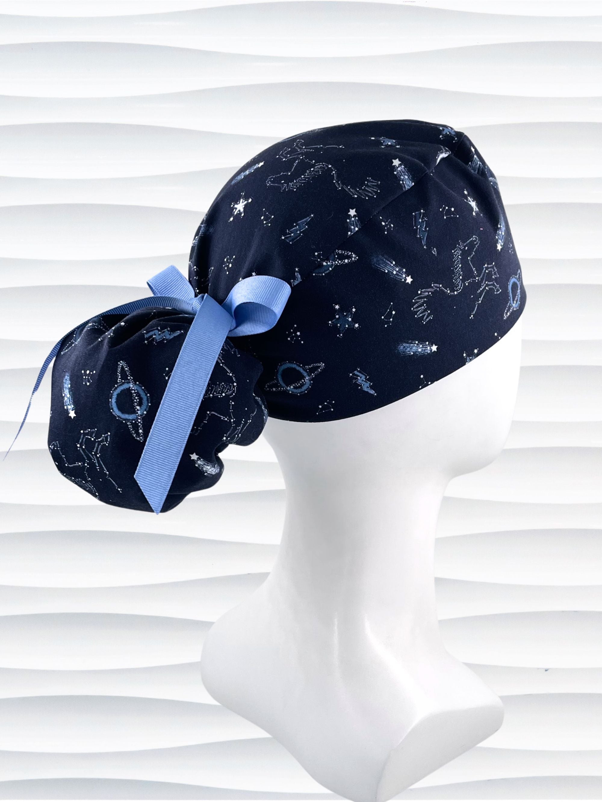 Ponytail style surgical scrub cap hat with stars, planets, and pegasus all over this dark blue cotton fabric.