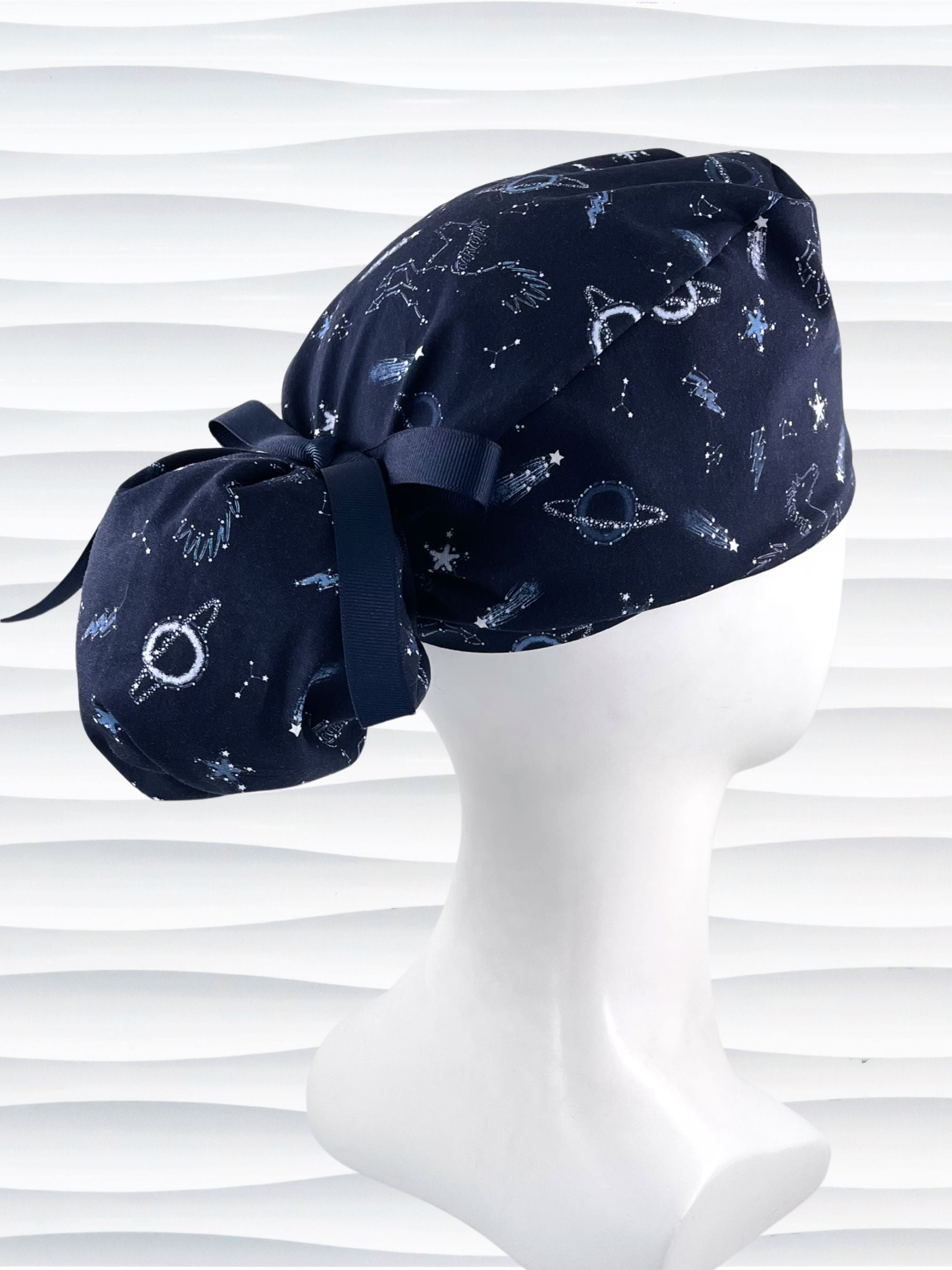 Ponytail style surgical scrub cap hat with stars, planets, and pegasus all over this dark blue cotton fabric.