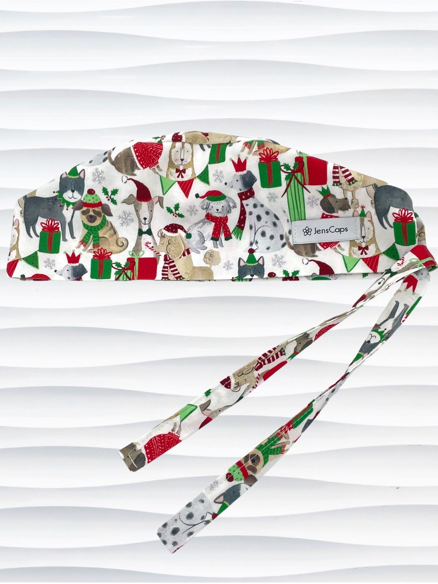 Mens surgeon style surgical scrub cap hat with dogs in scarves and santa hats in red, green, and white next to snowflakes and christmas presents on white cotton fabric.