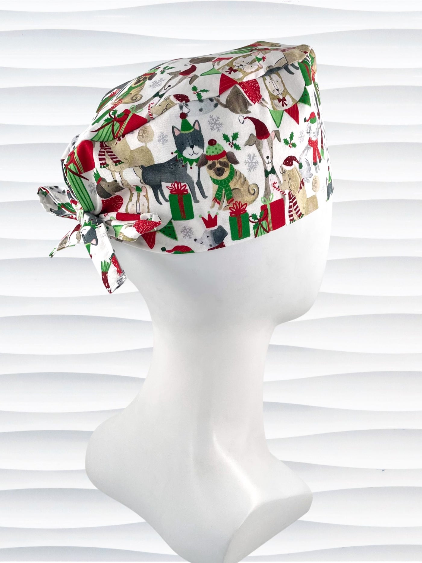 Mens surgeon style surgical scrub cap hat with dogs in scarves and santa hats in red, green, and white next to snowflakes and christmas presents on white cotton fabric.