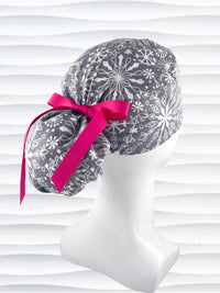 Ponytail style surgical scrub cap hat with white snowflakes all over a light gray cotton fabric.