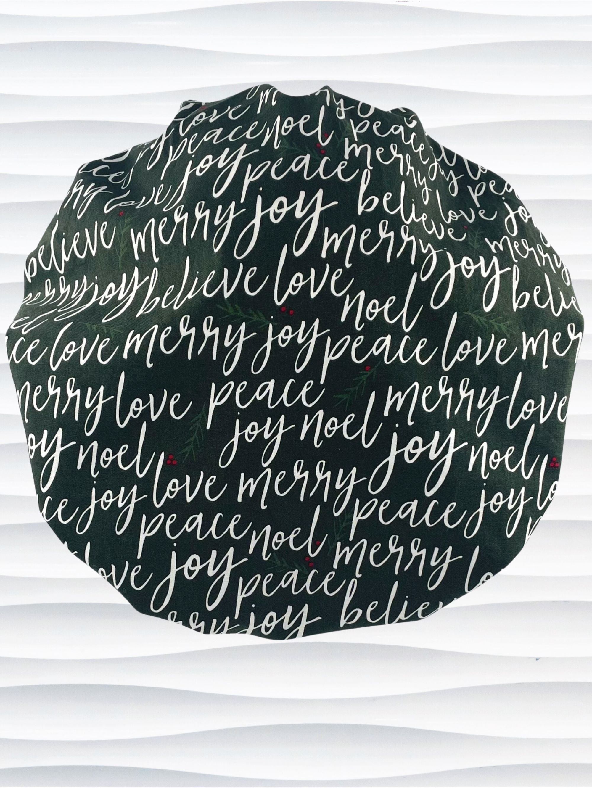 Bouffant style surgical scrub cap hat with love, merry, beleive, joy, peace and noel in a white script on dark green cotton fabric.