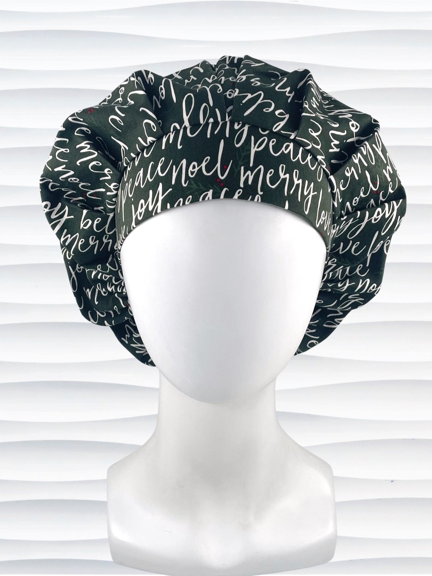 Bouffant style surgical scrub cap hat with love, merry, beleive, joy, peace and noel in a white script on dark green cotton fabric.