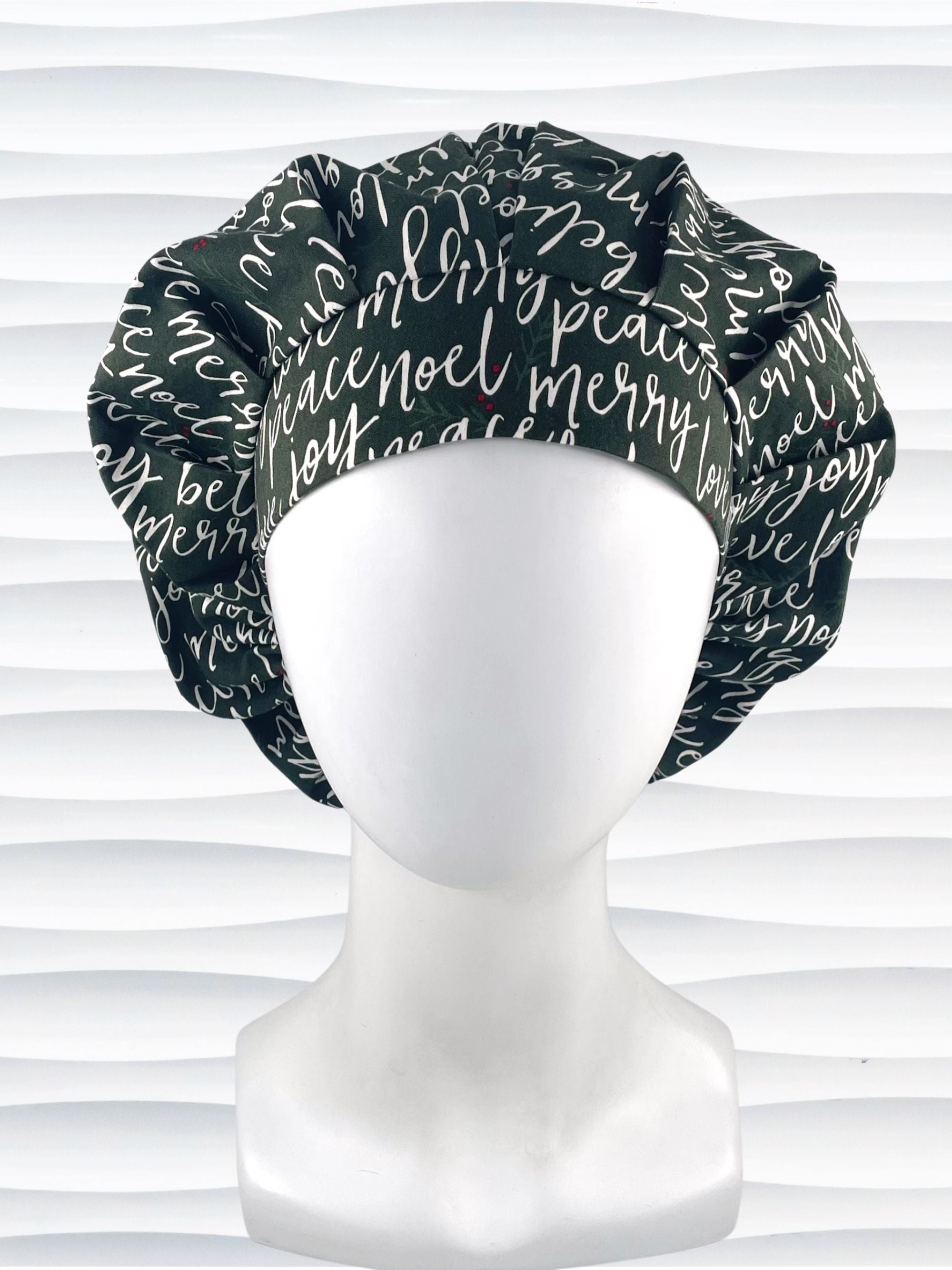 Bouffant style surgical scrub cap hat with love, merry, beleive, joy, peace and noel in a white script on dark green cotton fabric.