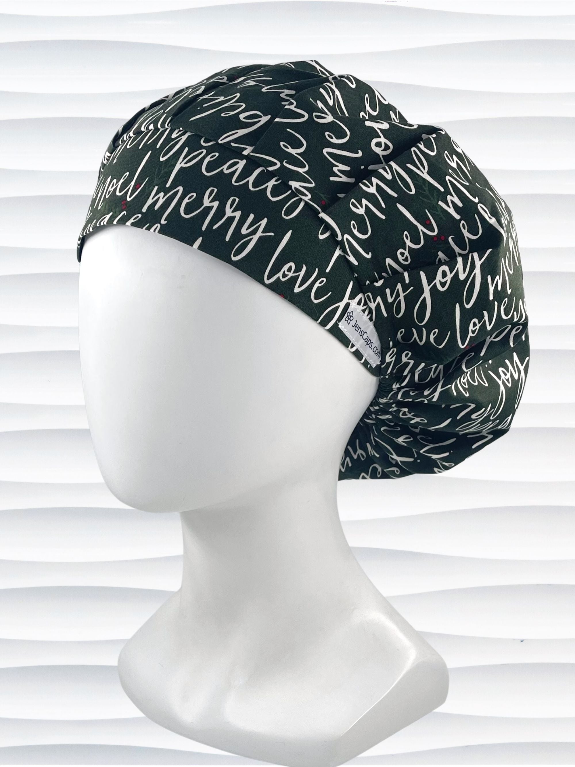 Bouffant style surgical scrub cap hat with love, merry, beleive, joy, peace and noel in a white script on dark green cotton fabric.