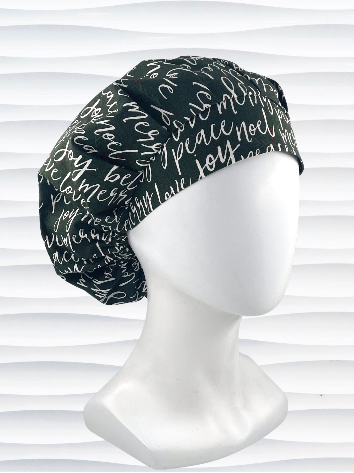 Bouffant style surgical scrub cap hat with love, merry, beleive, joy, peace and noel in a white script on dark green cotton fabric.