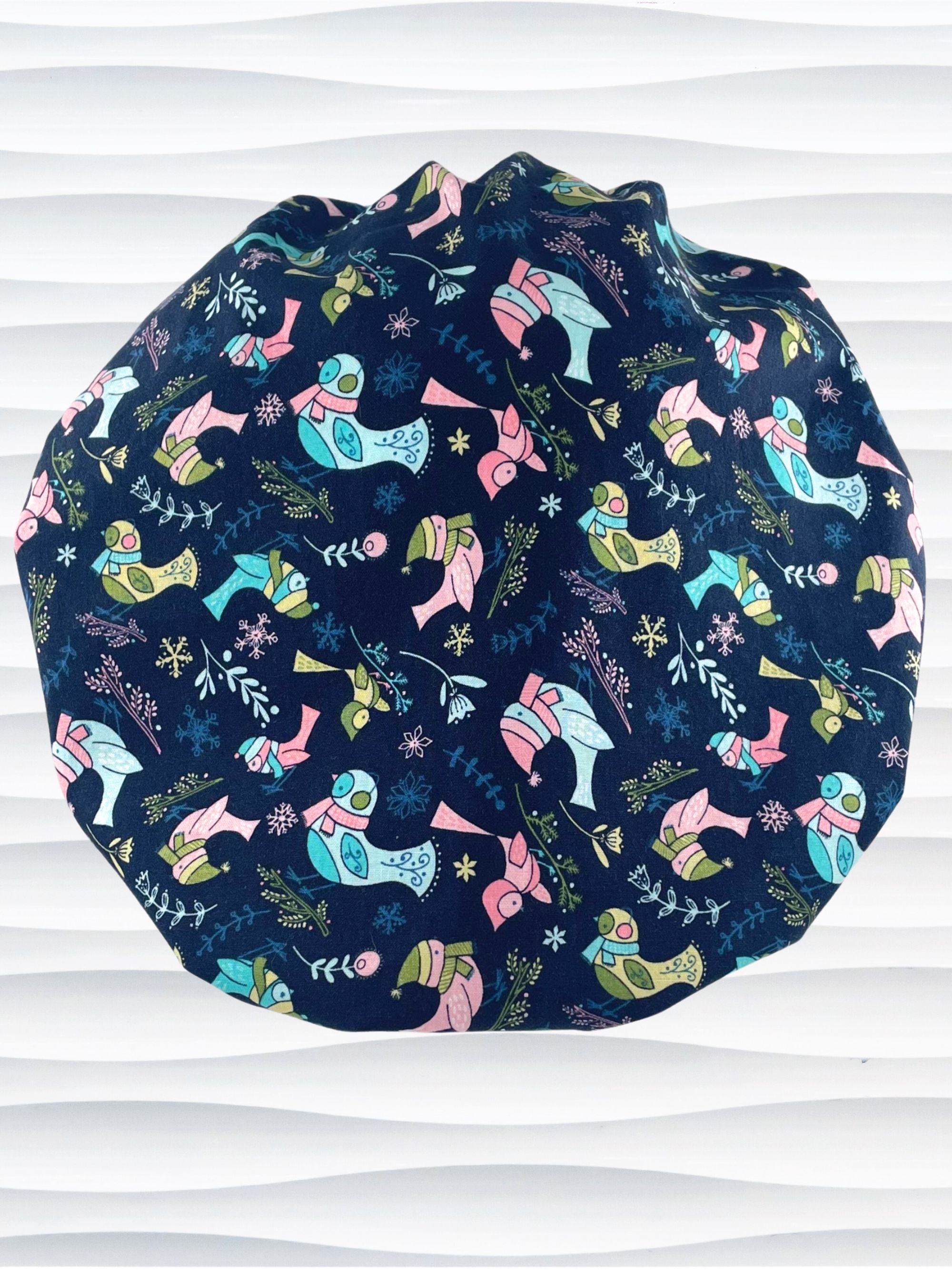 Bouffant style surgical scrub cap with pink and blue birds wearing ear muffs and scarves, snowflakes, and flowers on dark blue cotton fabric.