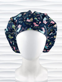 Bouffant style surgical scrub cap with pink and blue birds wearing ear muffs and scarves, snowflakes, and flowers on dark blue cotton fabric.