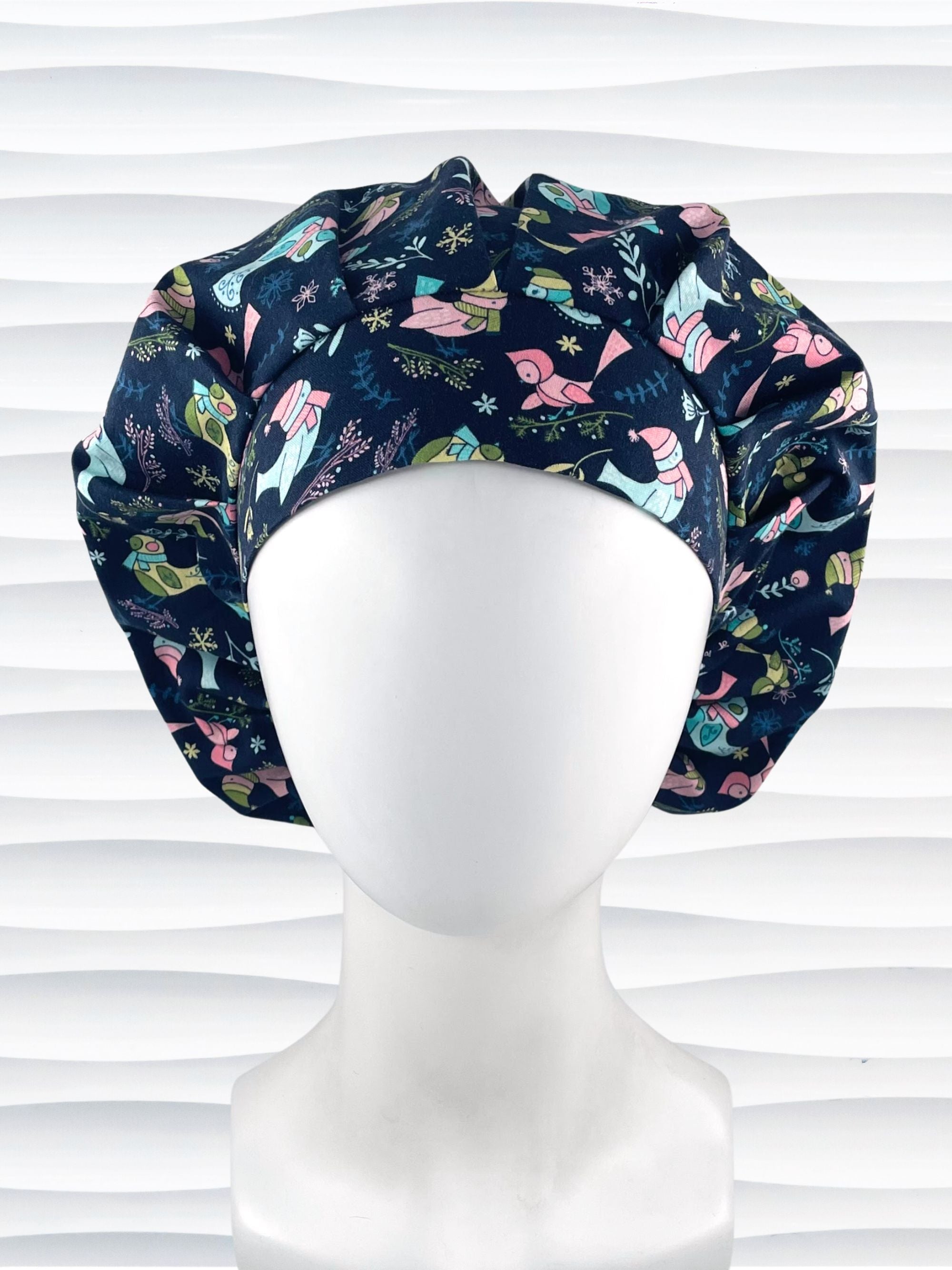 Bouffant style surgical scrub cap with pink and blue birds wearing ear muffs and scarves, snowflakes, and flowers on dark blue cotton fabric.