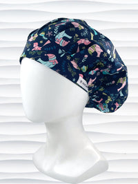 Bouffant style surgical scrub cap with pink and blue birds wearing ear muffs and scarves, snowflakes, and flowers on dark blue cotton fabric.