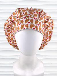 Bouffant style srugical scrub cap by Jenscaps made of white fabric patterned with repeating cute cartoon reindeer—some with pink bows—and red hearts, displayed against a white textured background.