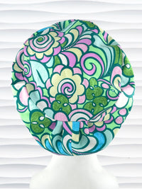 Euro Pixie style surgical scrub cap with a large and modern abstract floral print with swirls and butterflies in pinks, greens, and blues on cotton fabric.
