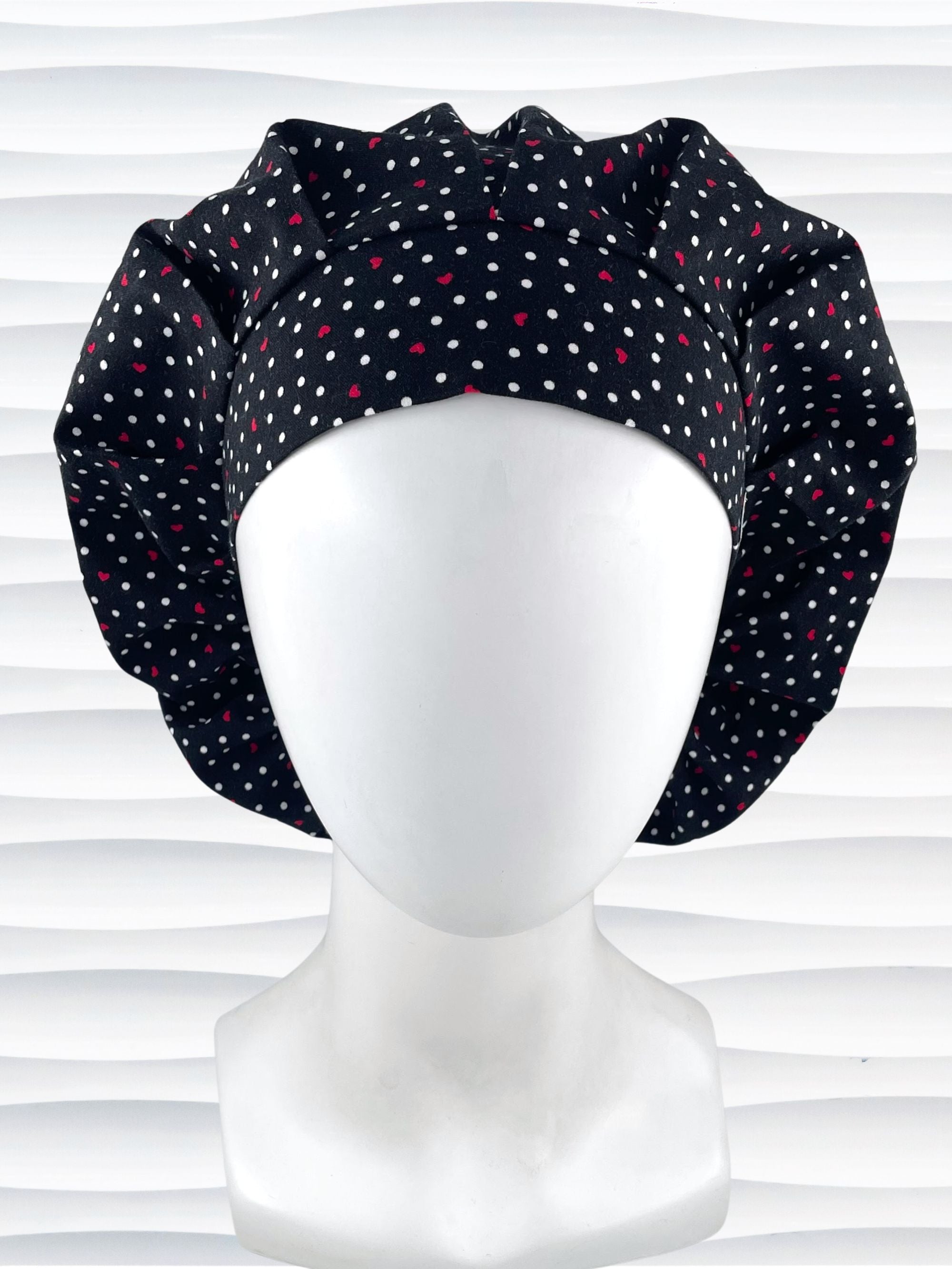 Bouffant style surgical scrub cap by JensCaps with small red hearts and white dots all over this black cotton fabric and displayed on a white mannequin head.