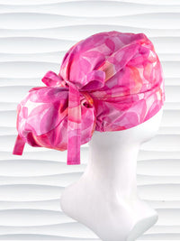 Euro Pony hybrid ponytail style surgical scrub cap by JensCaps with large flowers in light and dark pinks and peach sorbet on cotton fabric, finished with a ribbon tie and displayed on a mannequin head.