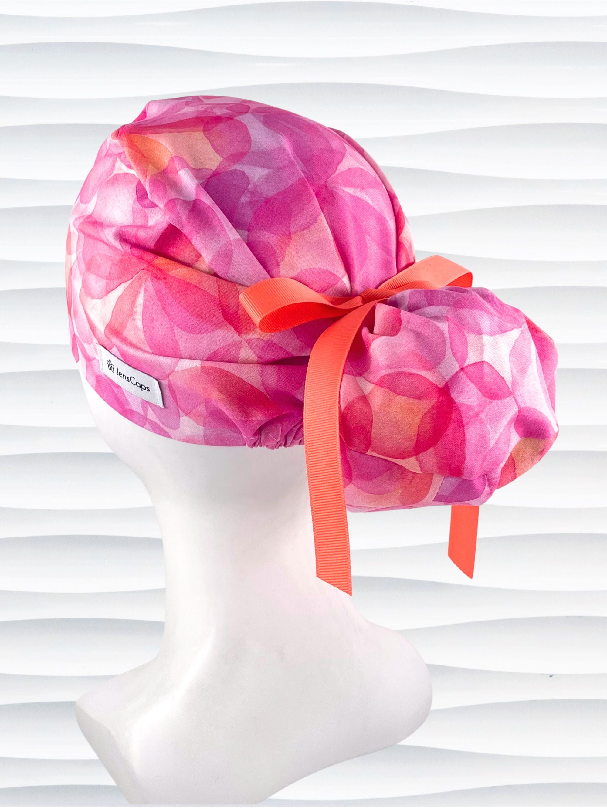 Euro Pony hybrid ponytail style surgical scrub cap by JensCaps with large flowers in light and dark pinks and peach sorbet on cotton fabric, finished with a ribbon tie and displayed on a mannequin head.