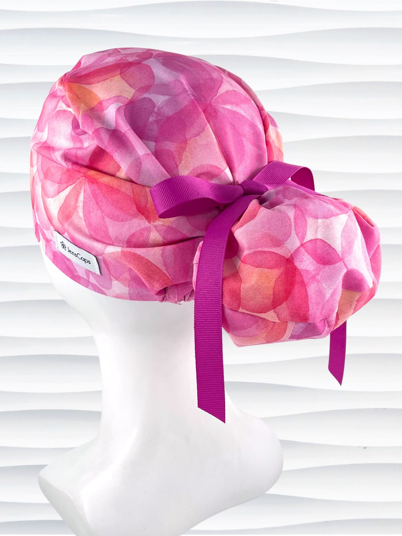 Euro Pony hybrid ponytail style surgical scrub cap by JensCaps with large flowers in light and dark pinks and peach sorbet on cotton fabric, finished with a ribbon tie and displayed on a mannequin head.