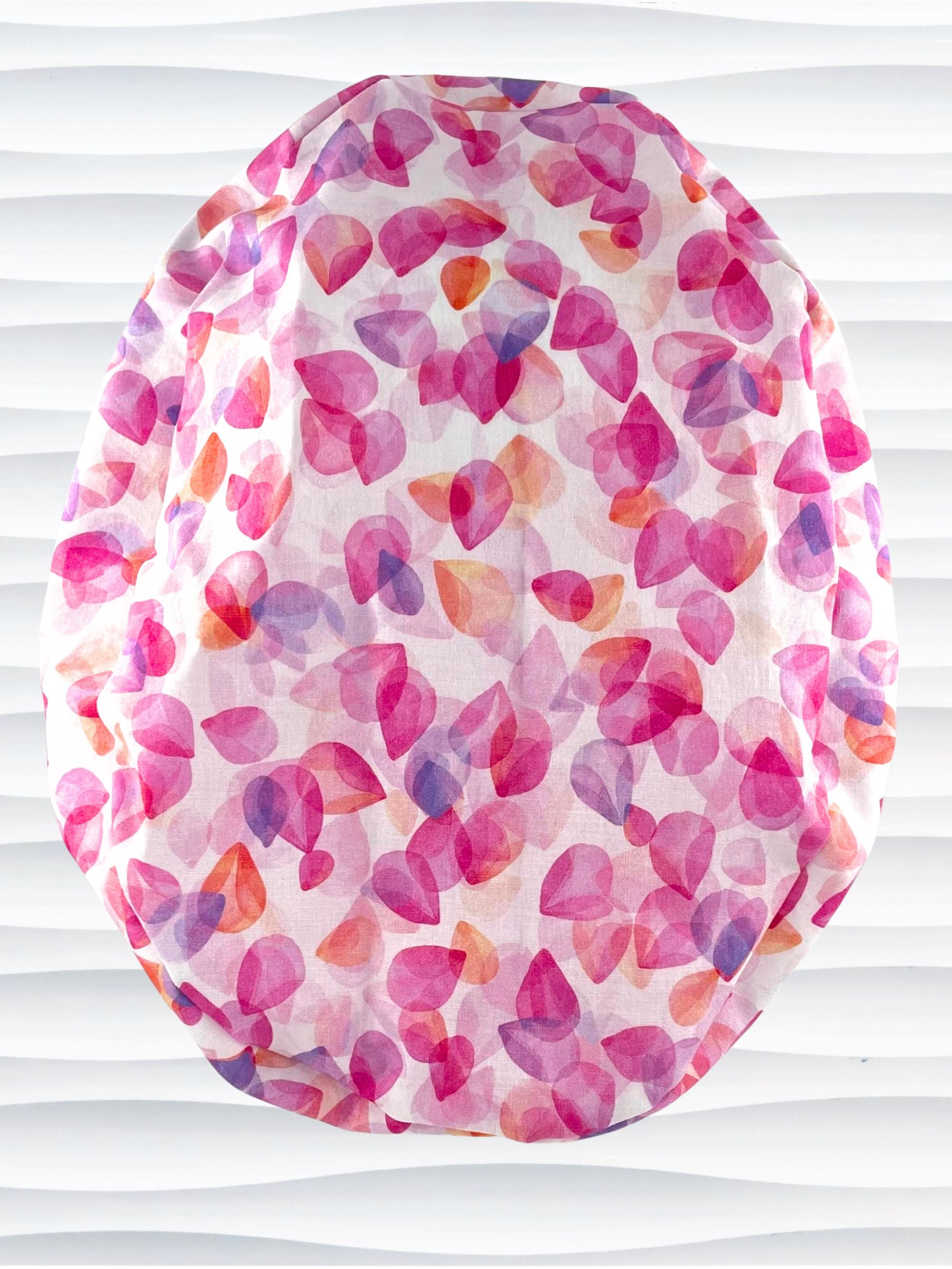 Euro Pony style surgical scrub cap with pink, purple, orange pastel colored flower petals tossed on white cotton fabric.