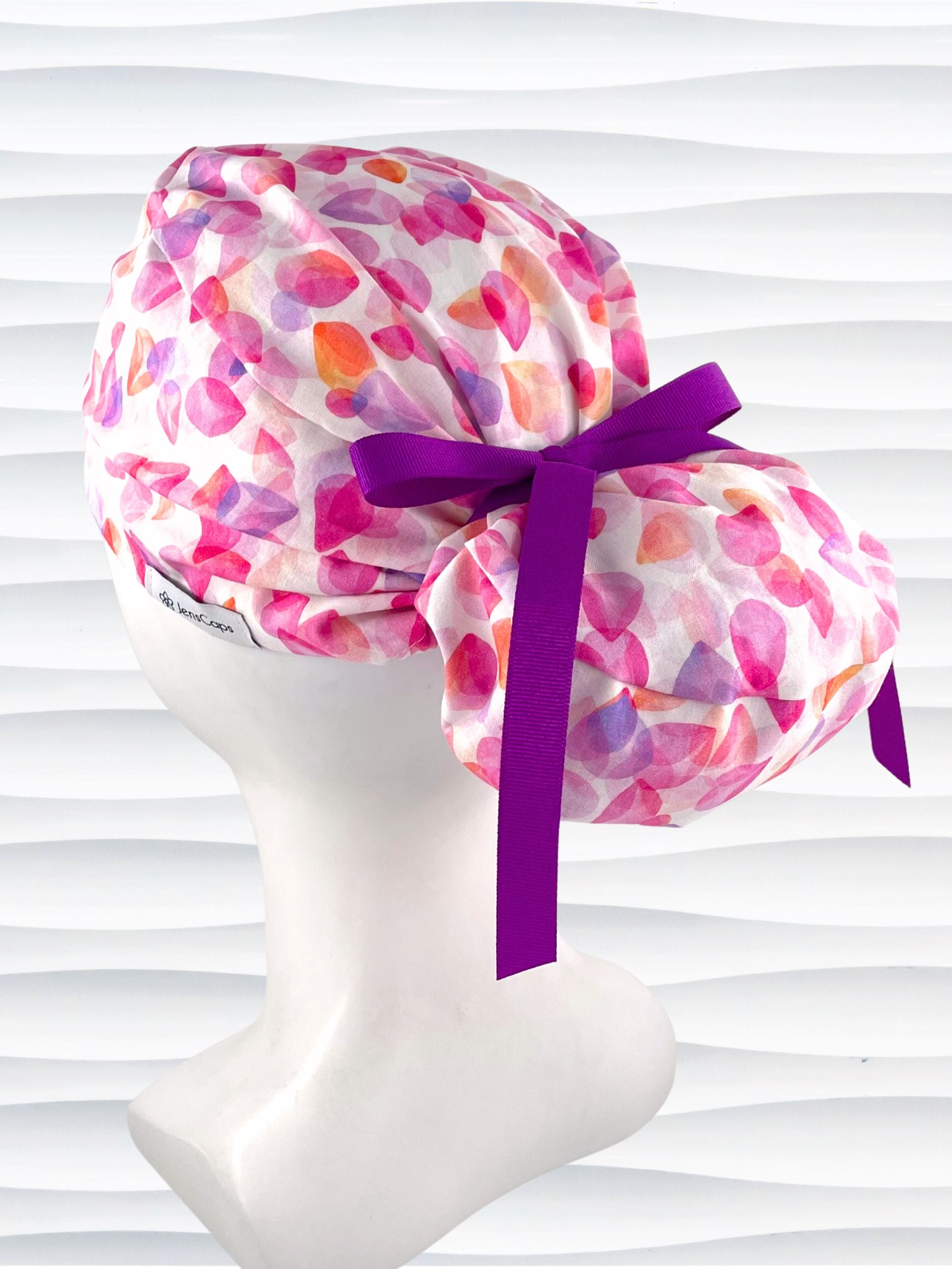 Euro Pony style surgical scrub cap with pink, purple, orange pastel colored flower petals tossed on white cotton fabric.