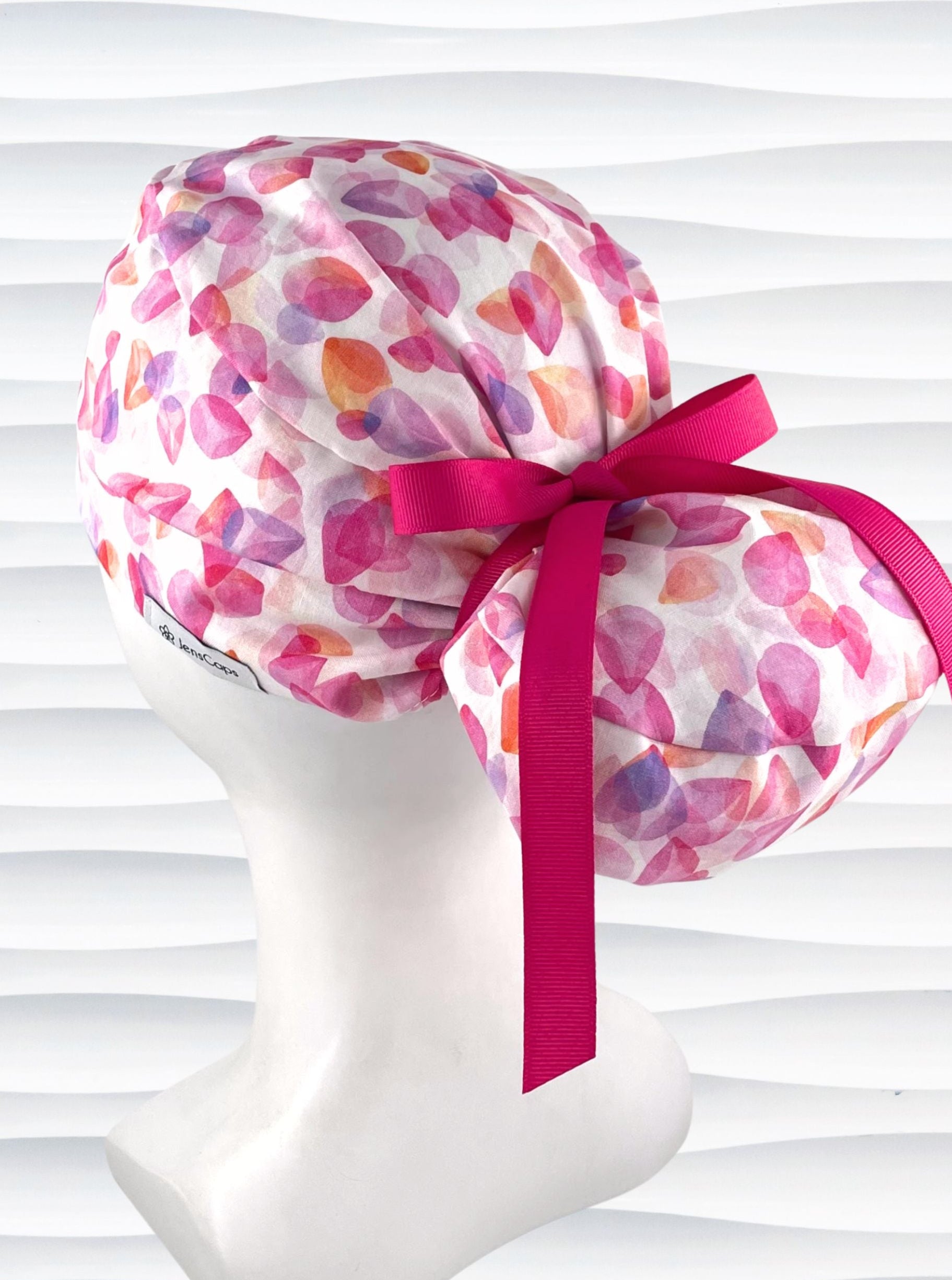 Euro Pony style surgical scrub cap with pink, purple, orange pastel colored flower petals tossed on white cotton fabric.