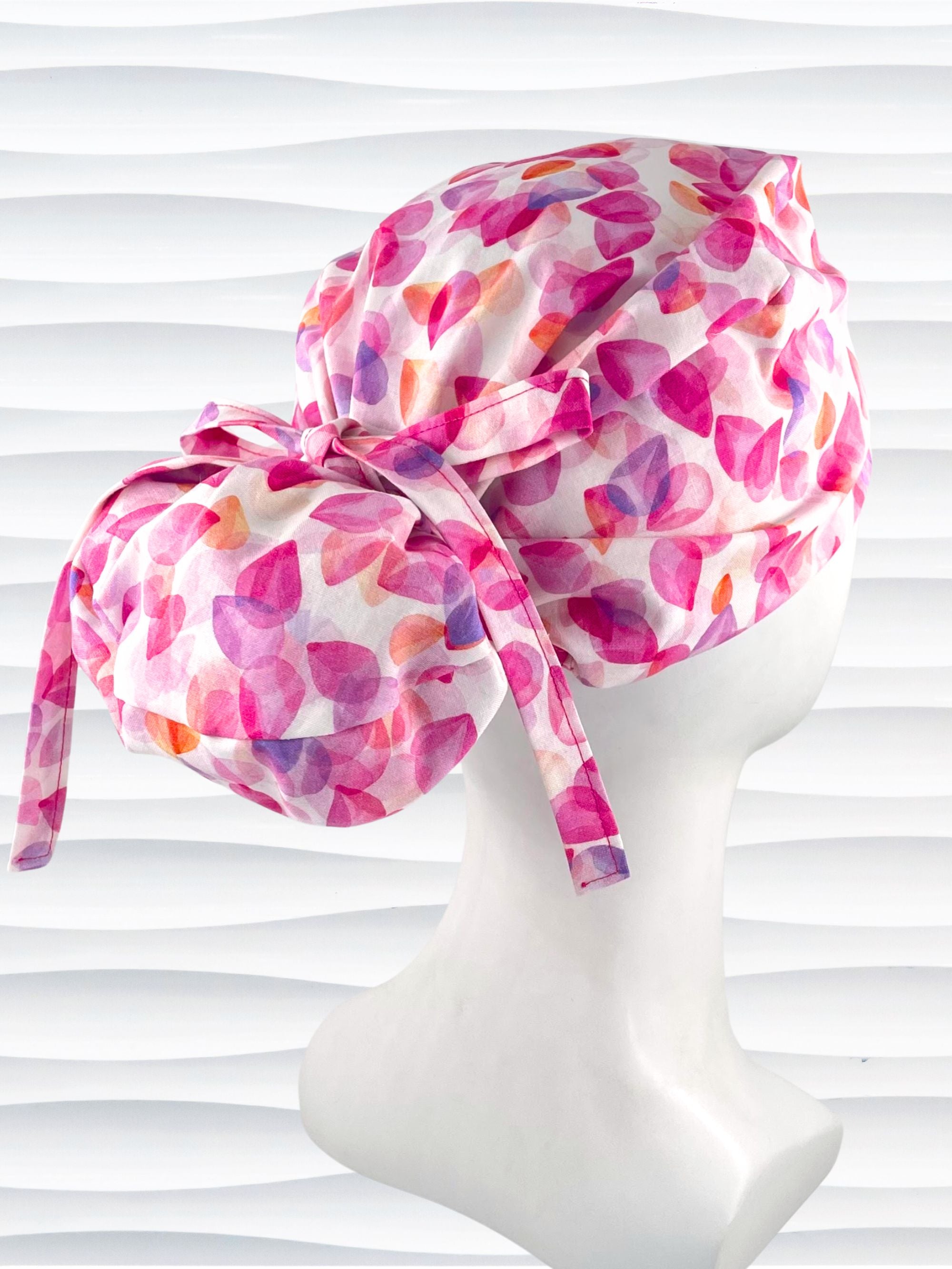 Euro Pony style surgical scrub cap with pink, purple, orange pastel colored flower petals tossed on white cotton fabric.