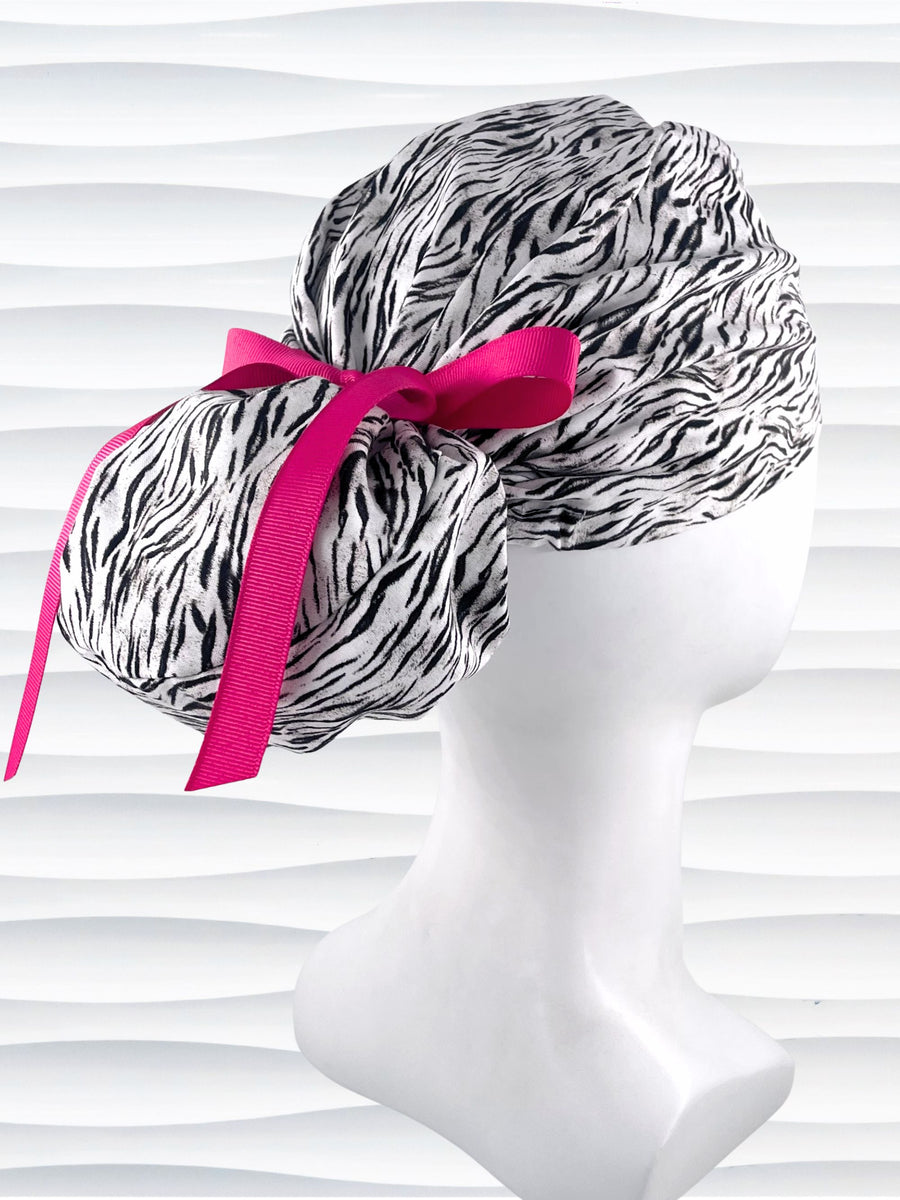 Euro style ponytail surgical scrub cap by JensCaps with a black and white zebra or snow tiger animal print on cotton fabric, finished with a grosgrain ribbon tie., and displayed on a white mannequin head.