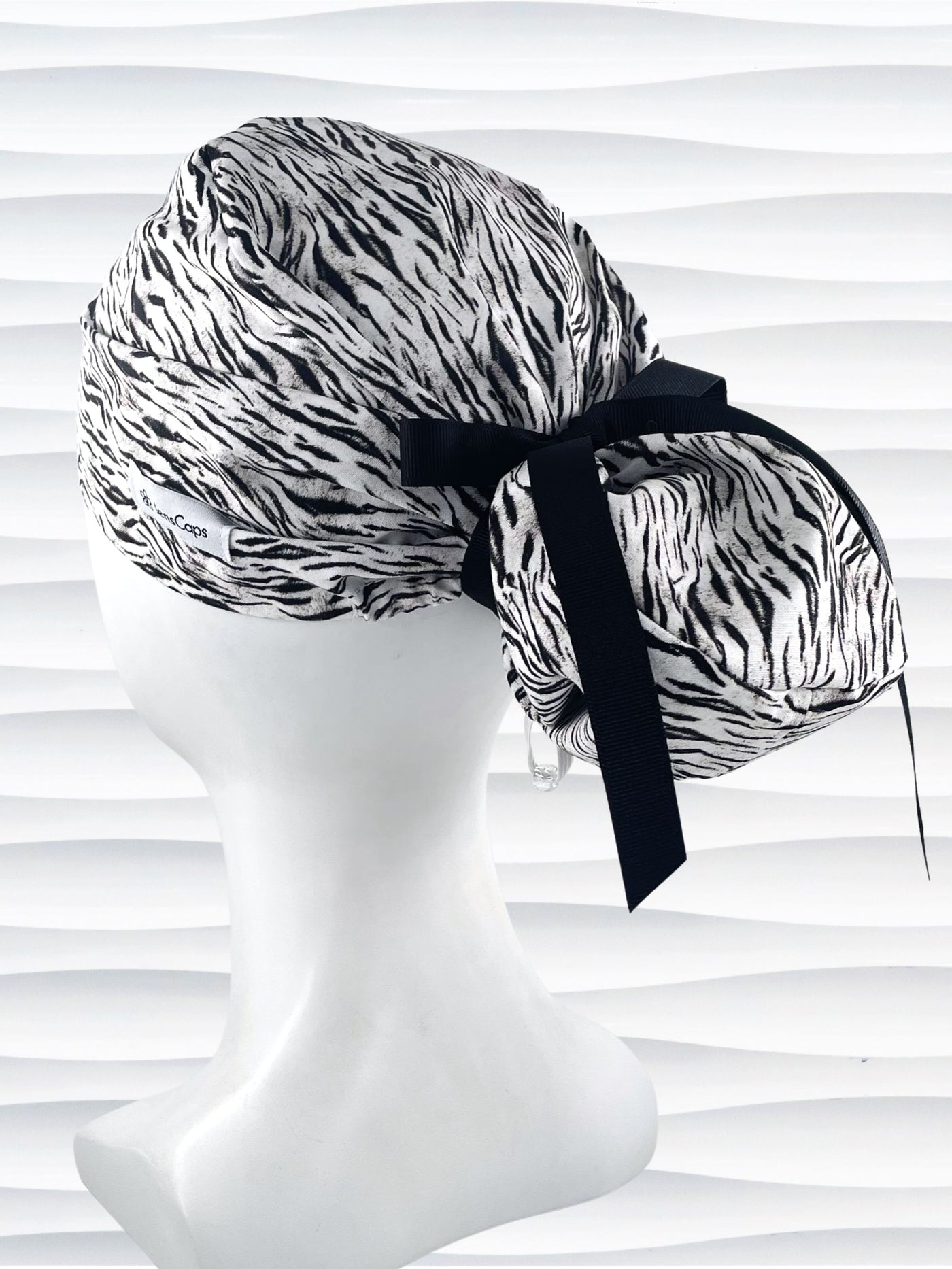 Euro style ponytail surgical scrub cap by JensCaps with a black and white zebra or snow tiger animal print on cotton fabric, finished with a grosgrain ribbon tie., and displayed on a white mannequin head.