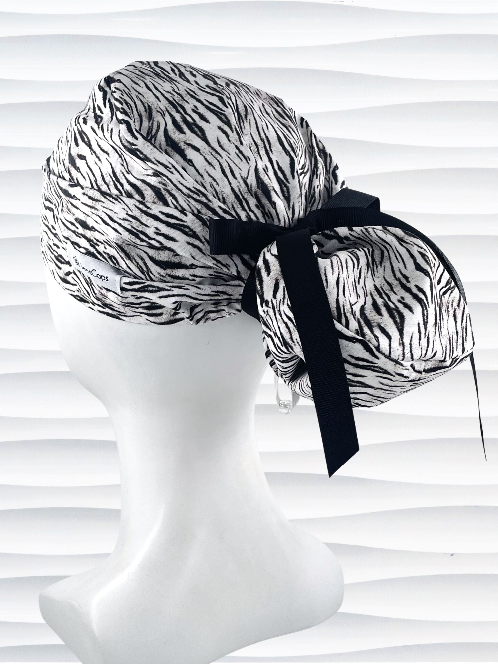 Euro style ponytail surgical scrub cap by JensCaps with a black and white zebra or snow tiger animal print on cotton fabric, finished with a grosgrain ribbon tie., and displayed on a white mannequin head.