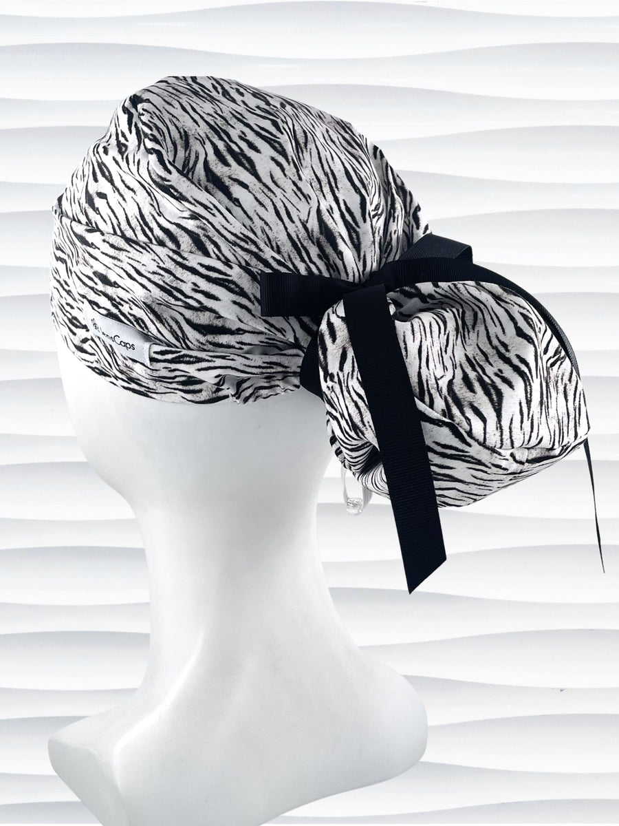 Euro style ponytail surgical scrub cap by JensCaps with a black and white zebra or snow tiger animal print on cotton fabric, finished with a grosgrain ribbon tie., and displayed on a white mannequin head.