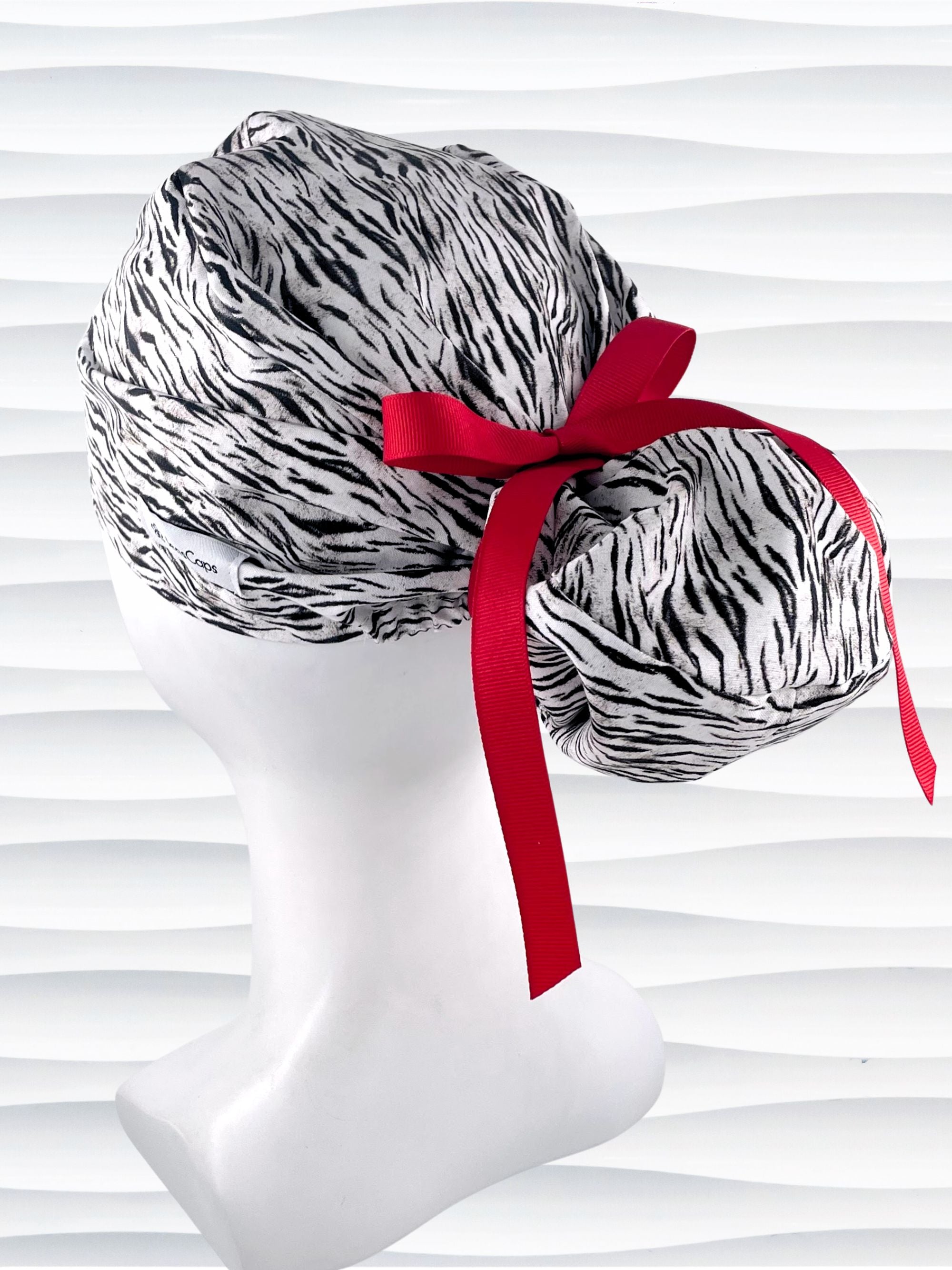 Euro style ponytail surgical scrub cap by JensCaps with a black and white zebra or snow tiger animal print on cotton fabric, finished with a grosgrain ribbon tie., and displayed on a white mannequin head.