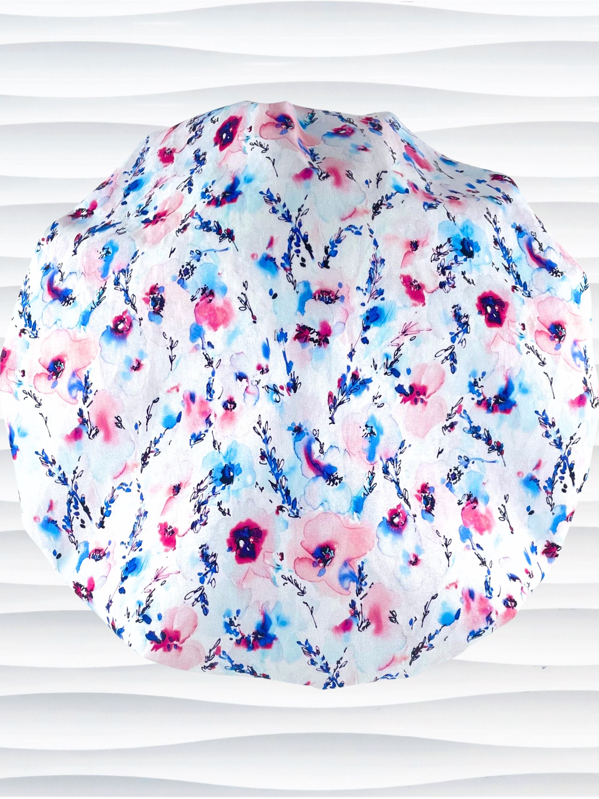 Bouffant style surgical scrub cap with watercolor looking pink and blue flowers and stems on white cotton fabric.