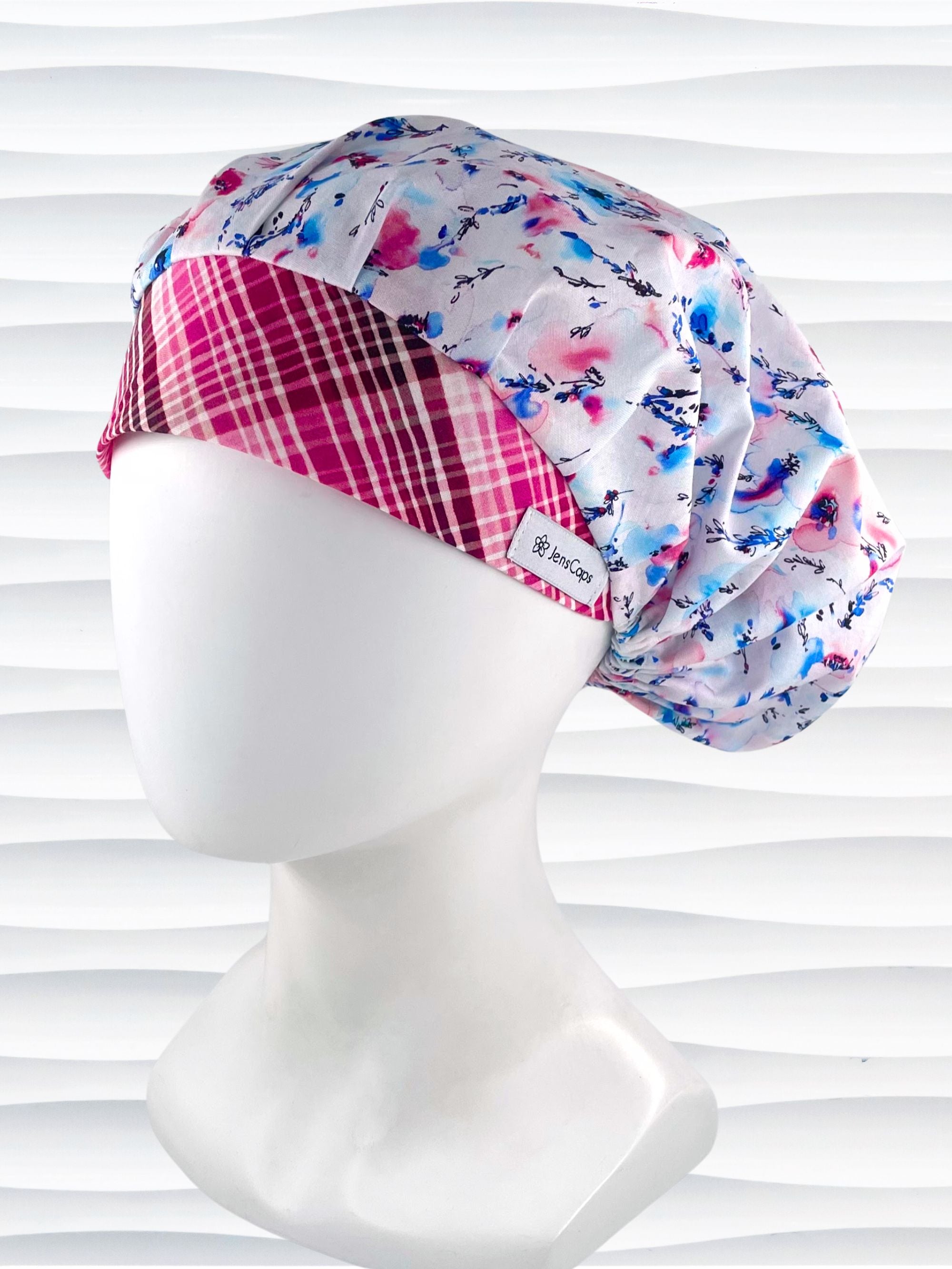 Bouffant style surgical scrub cap with watercolor looking pink and blue flowers and stems on white cotton fabric.