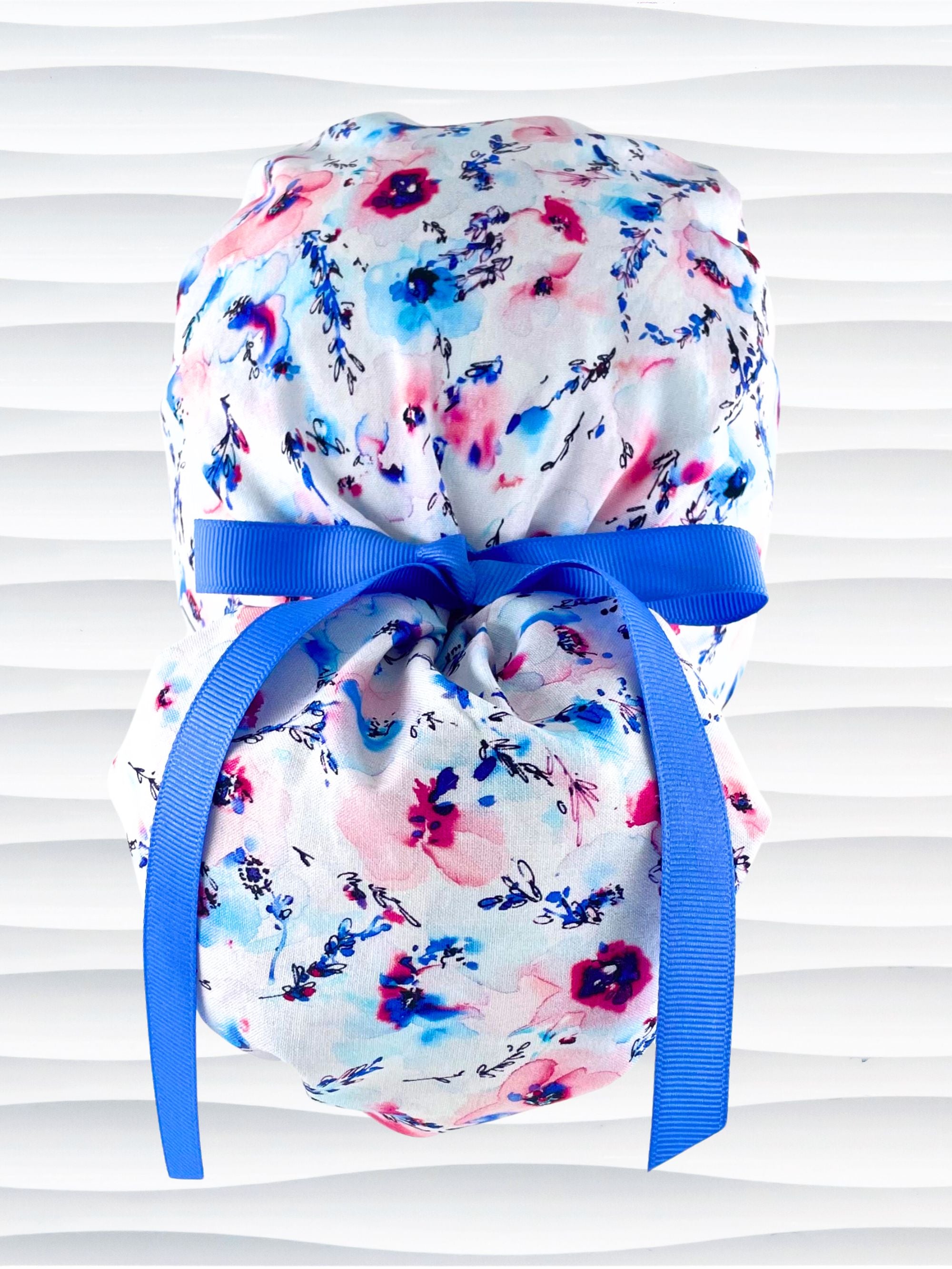Ponytail style surgical scrub cap with abstract flowers in pinks and blues all over white premium cotton fabric and finished with grosgrain ribbon ties.