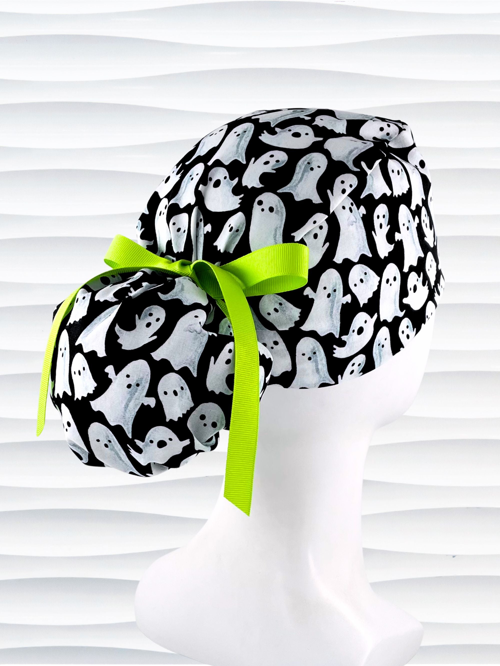 Ponytail style surgical scrub cap with animated white ghosts tossed all over black cotton fabric and finished with grosgrain ribbon ties.