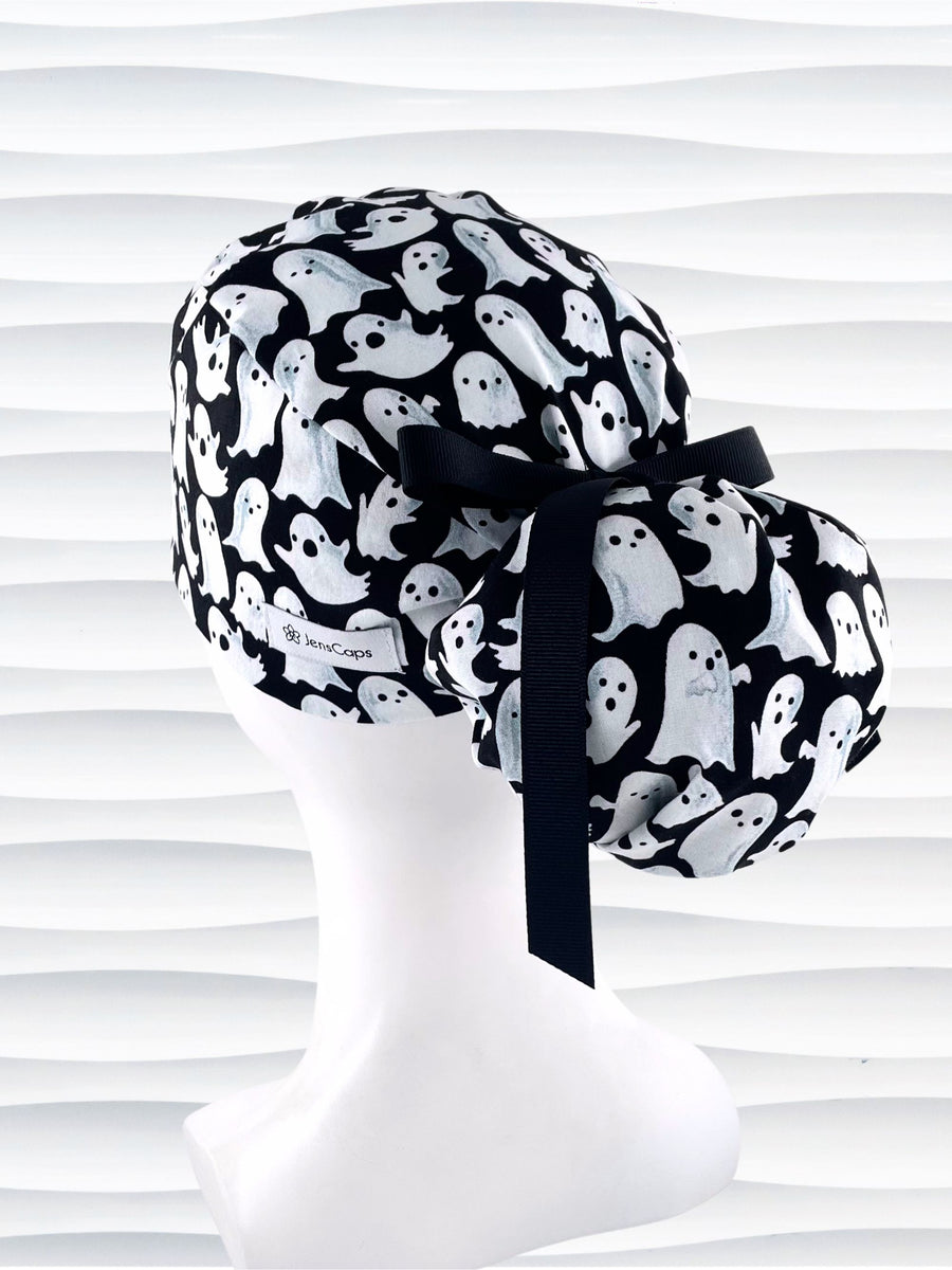 Ponytail style surgical scrub cap with animated white ghosts tossed all over black cotton fabric and finished with grosgrain ribbon ties.