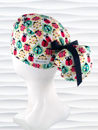 Ponytail style surgical scrub cap with ladybugs and flowers in a retro theme on cotton fabric and finished with a grosgrain ribbon.
