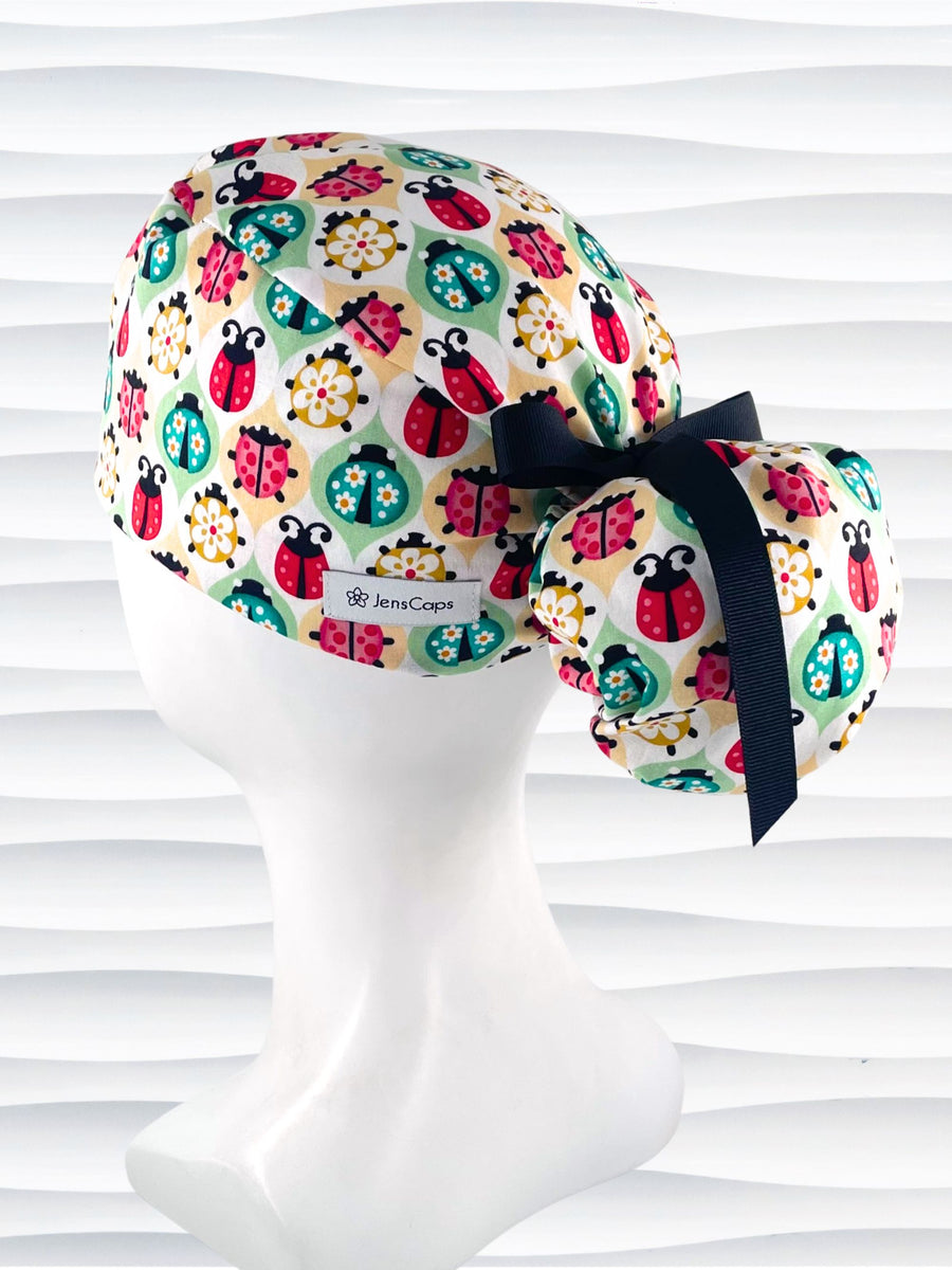 Ponytail style surgical scrub cap with ladybugs and flowers in a retro theme on cotton fabric and finished with a grosgrain ribbon.