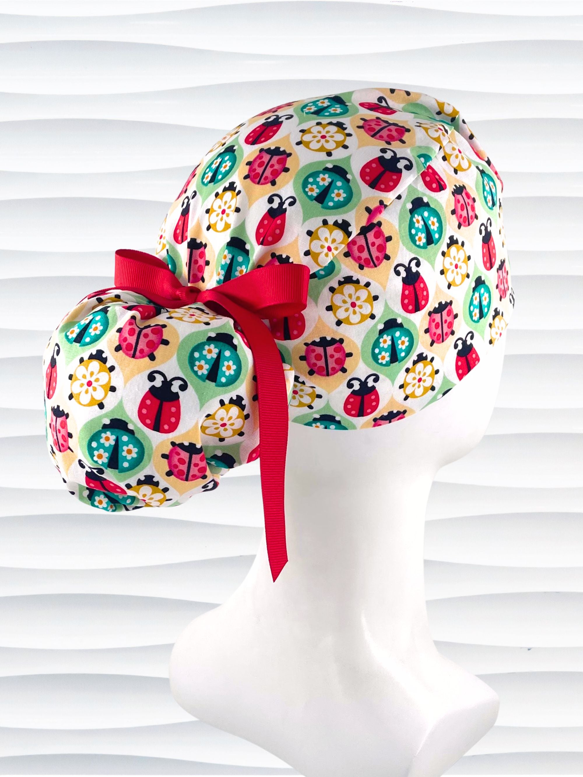 Ponytail style surgical scrub cap with ladybugs and flowers in a retro theme on cotton fabric and finished with a grosgrain ribbon.