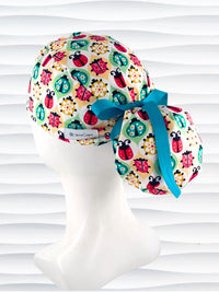 Ponytail style surgical scrub cap with ladybugs and flowers in a retro theme on cotton fabric and finished with a grosgrain ribbon.