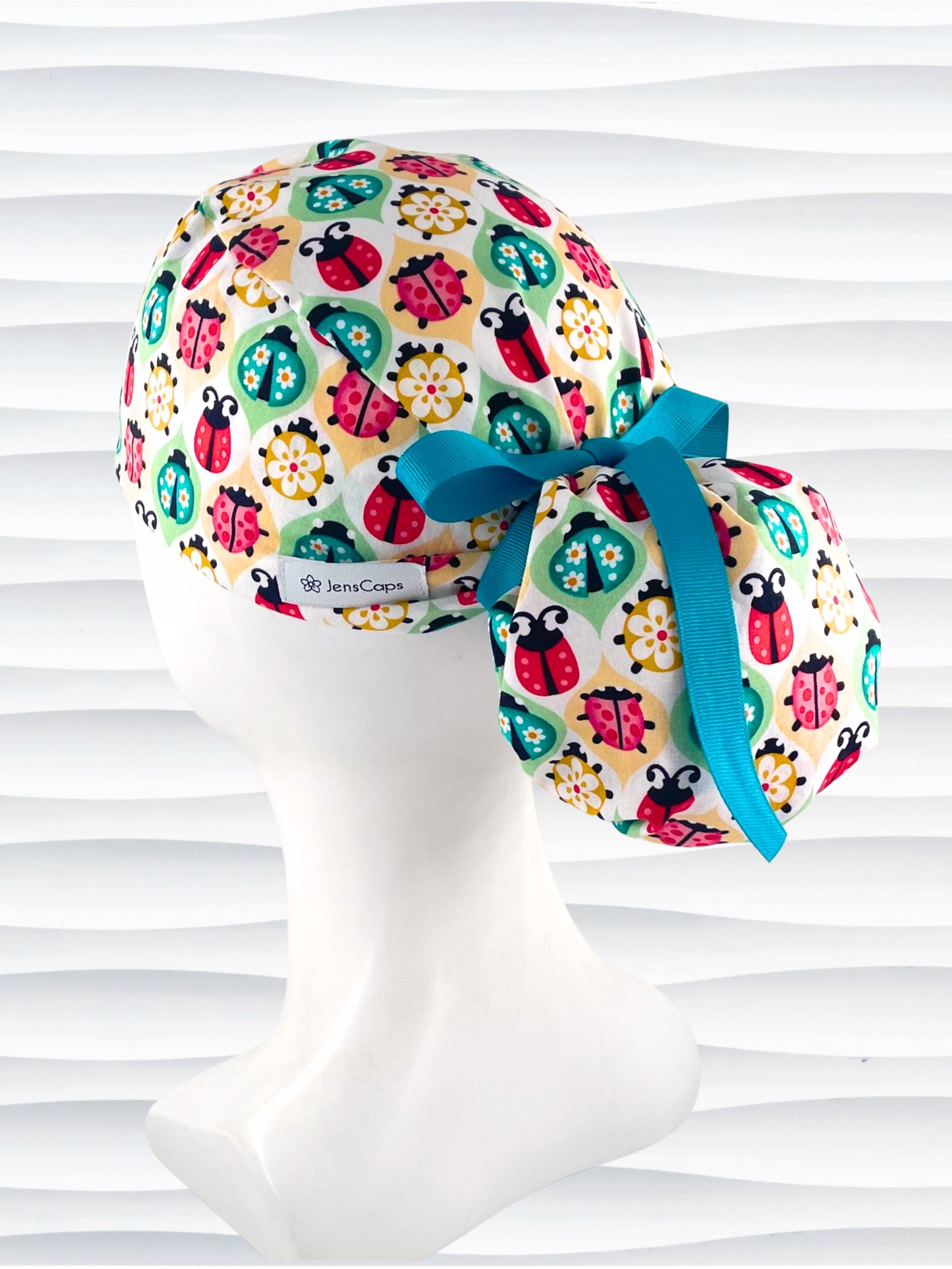 Ponytail style surgical scrub cap with ladybugs and flowers in a retro theme on cotton fabric and finished with a grosgrain ribbon.