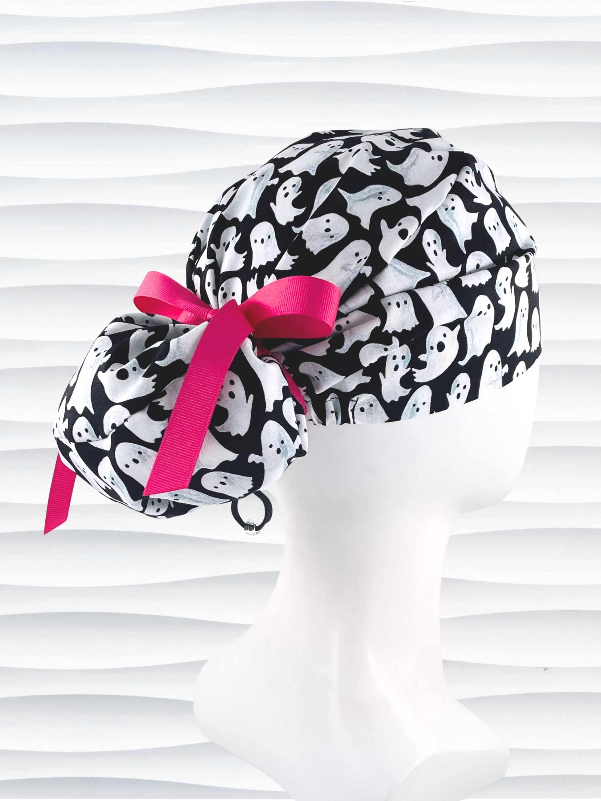 Euro Pony style surgical ponytail scrub cap with friendly white ghosts tossed all over black cotton fabric and finished with grosgrain ribbon ties.