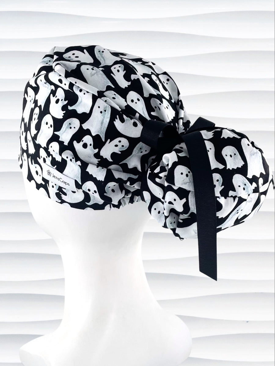 Euro Pony style surgical ponytail scrub cap with friendly white ghosts tossed all over black cotton fabric and finished with grosgrain ribbon ties.